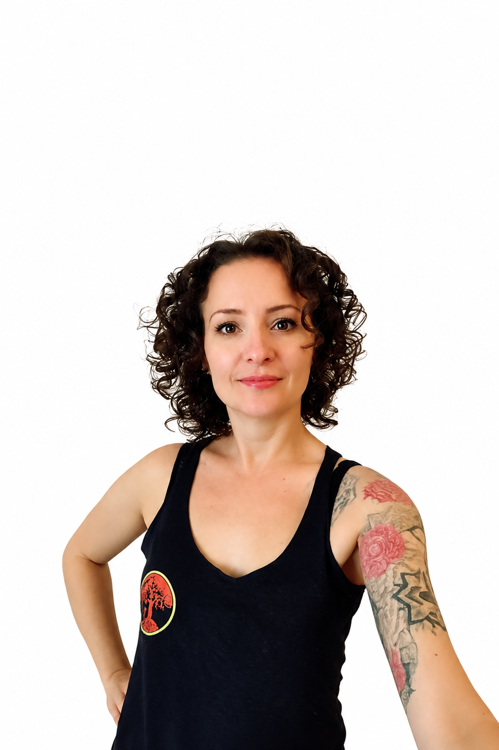 Woman with short curly hair in a black sleeveless top, tattoo sleeve on her right arm, posing against a white background.