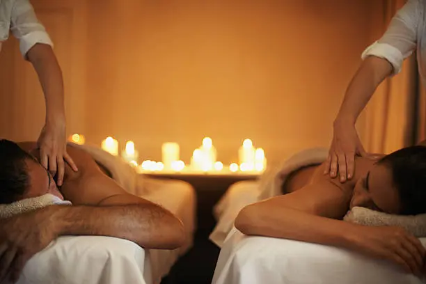 Deux masseurs travaillent sur des clients allongés, ambiance chaude avec bougies en arrière-plan dans un spa. Deux masseurs travaillent sur des clients allongés, ambiance chaude avec bougies en arrière-plan dans un spa.