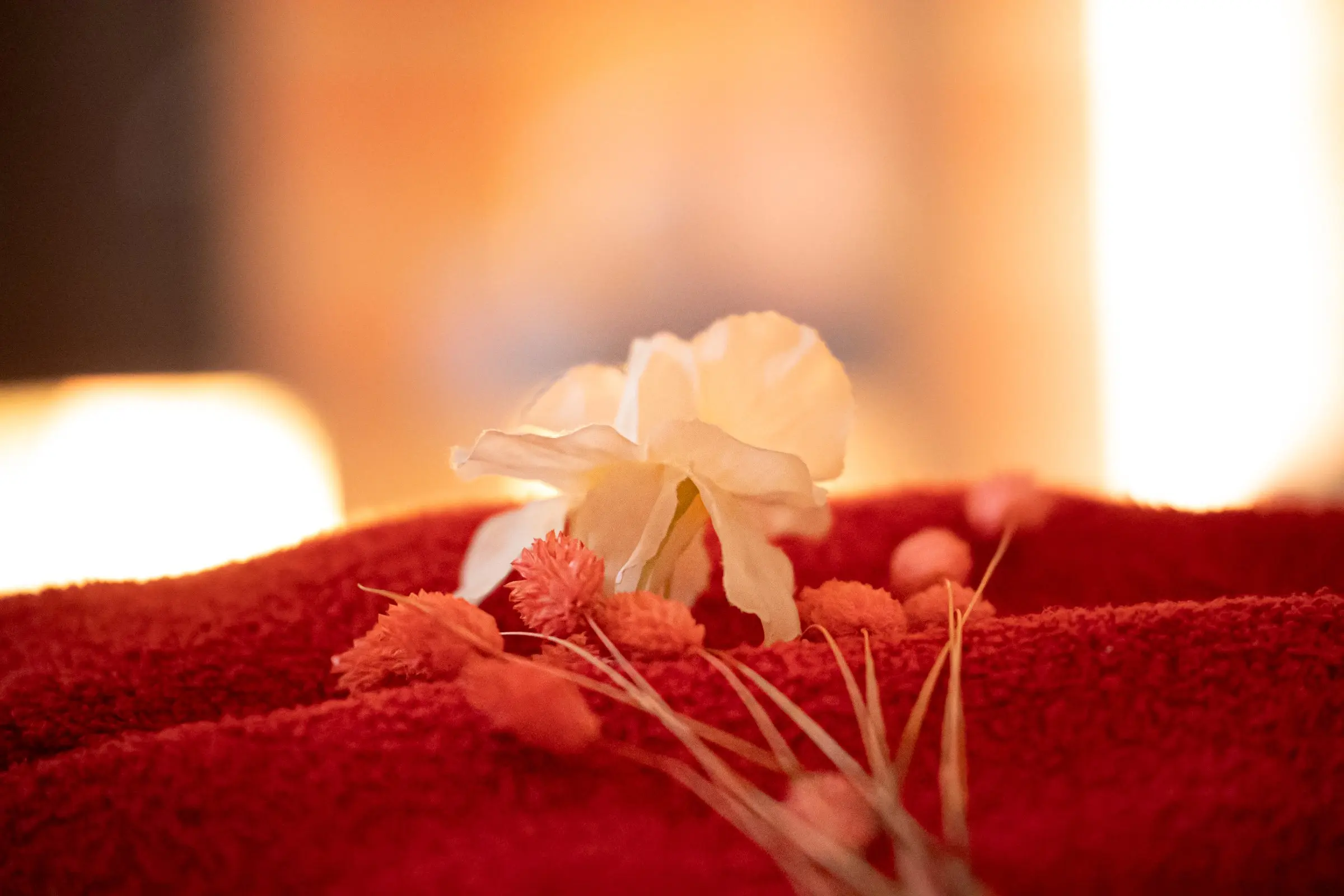 Parment d’ambiance d’un spa: fleur blanche sur une serviette rouge, décor chaleureux et lumière douce.