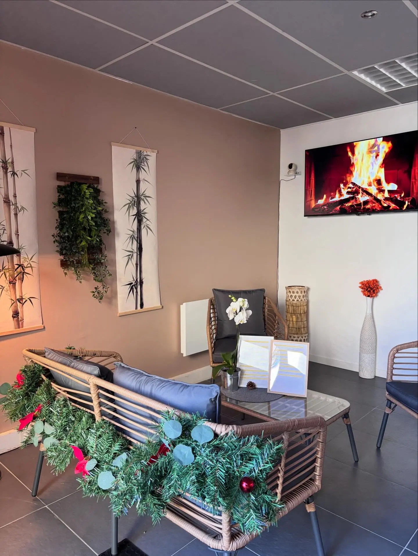 Salon cosy avec canapés en rotin, décor végétal et cheminée écran, ambiance lounge pour l’accueil clients.