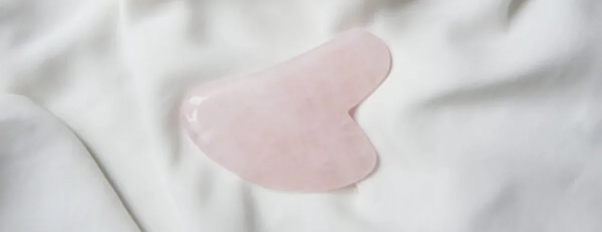 Un gua sha de quartz rose posé sur une soie claire